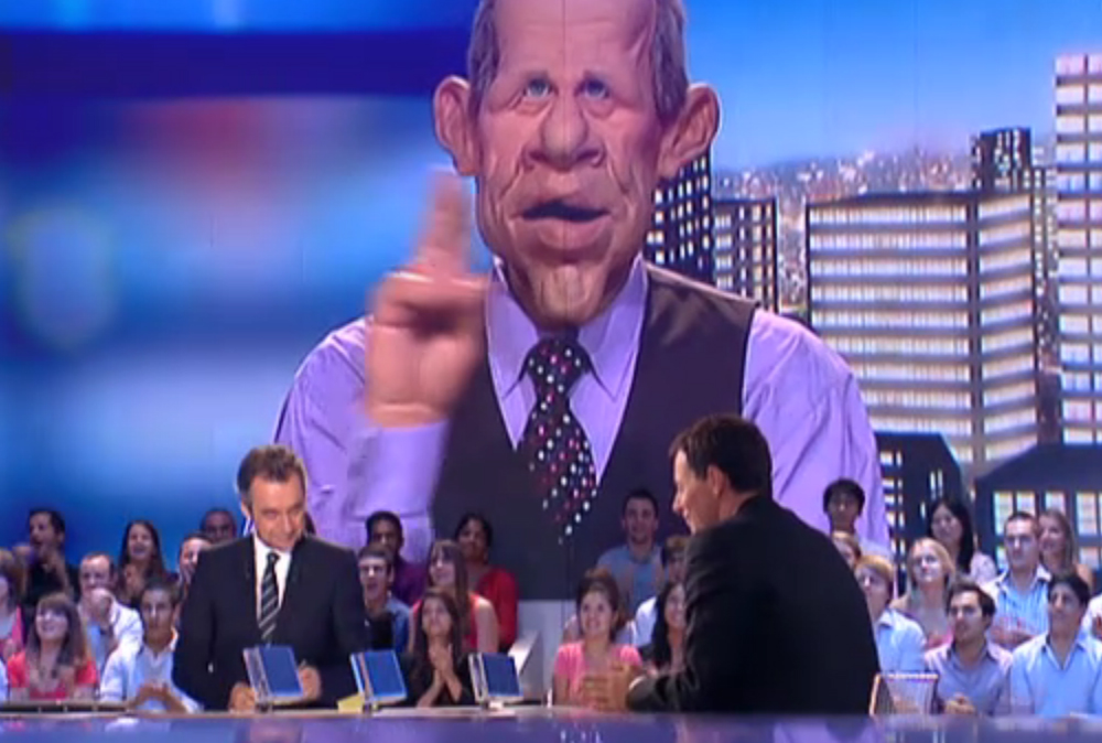 The anchor of Les Guignols de l'Info as the program transitions back to the roundtable discussion