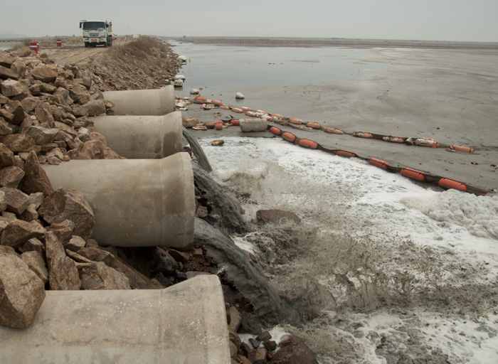 Pipes draining water from other side of dike. A dump truck in the background carries earth for the next dike.